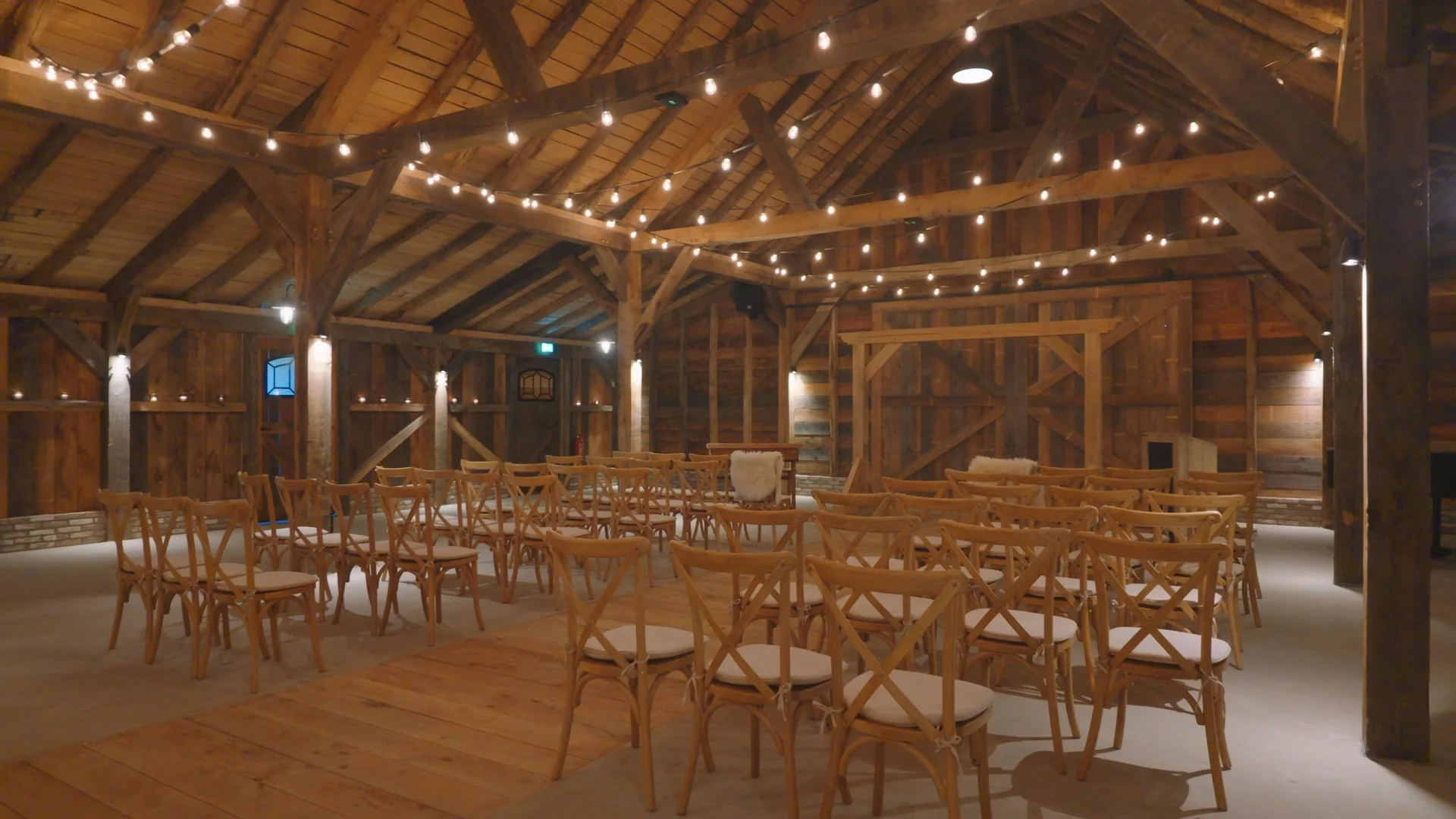 The Barn in opstelling: rijen houten stoelen en tafels onder de eiken spanten, met lichtsnoeren tussen de gebinten.